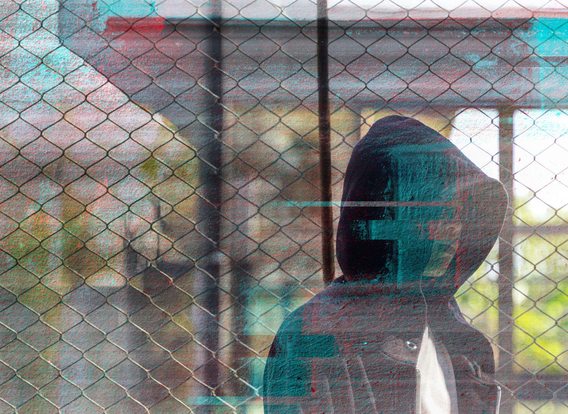 hooded teen stands behind chain link fence