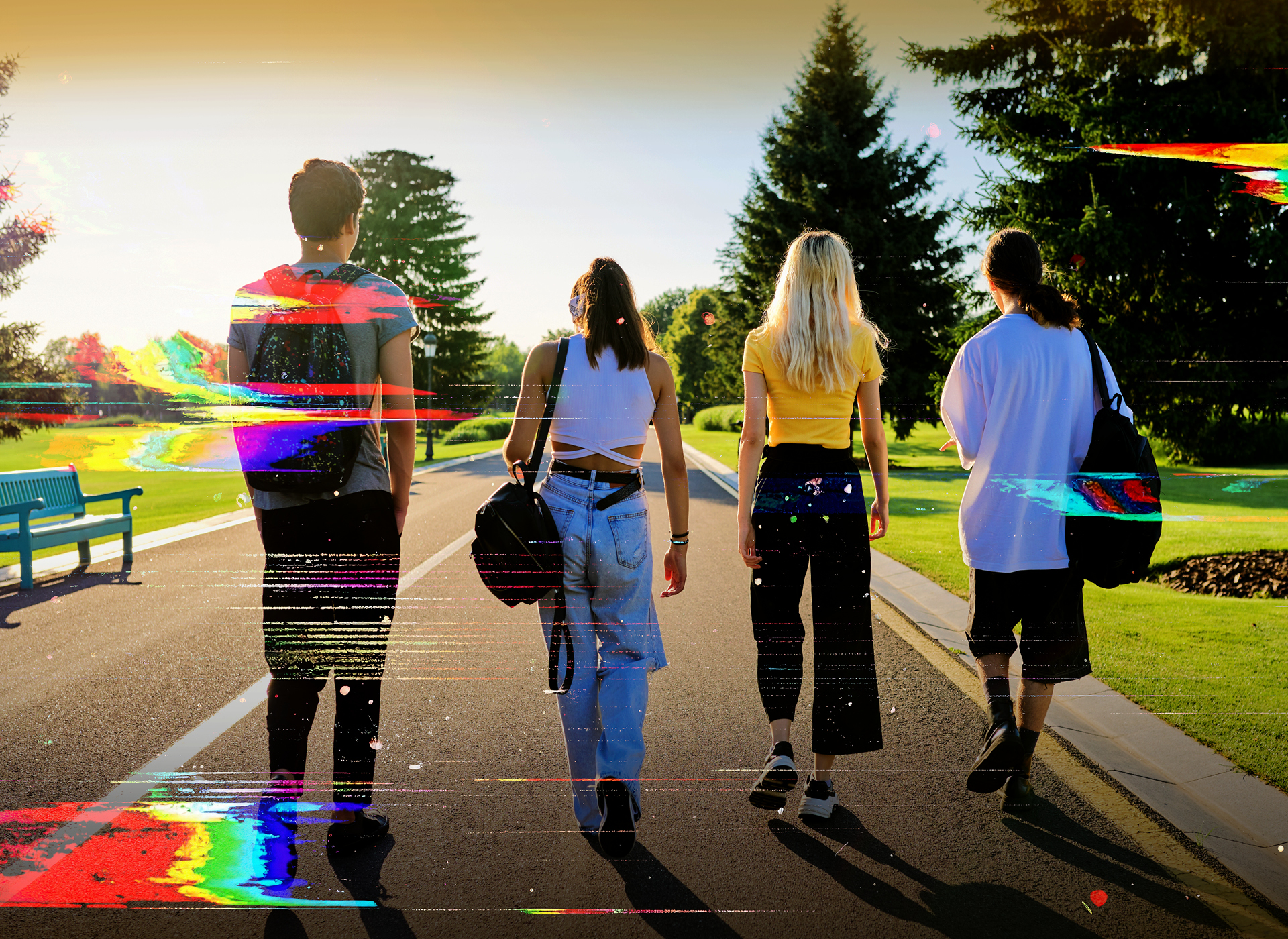 four teens with their backs to the camera walk down a road