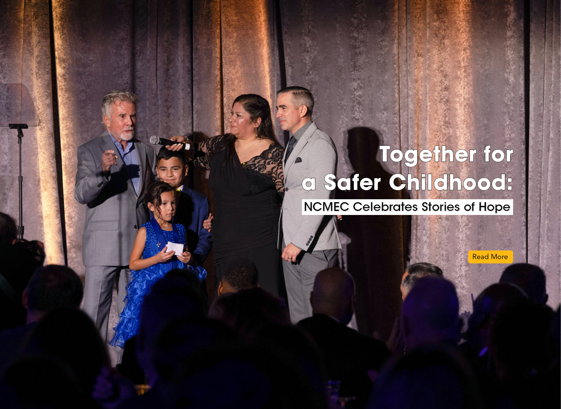 john and callahan walsh both in gray suits stand on stage with woman in black gown, boy in blue suit, and girl in blue dress
